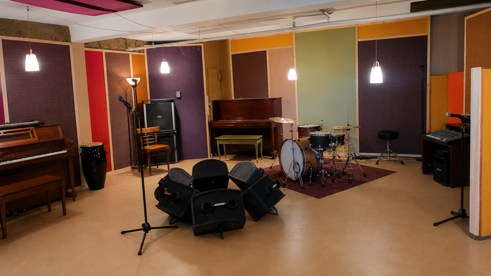 The Loft rehearsal studio featuring a piano, drum kit, PA monitors, and colorful acoustic wall panels